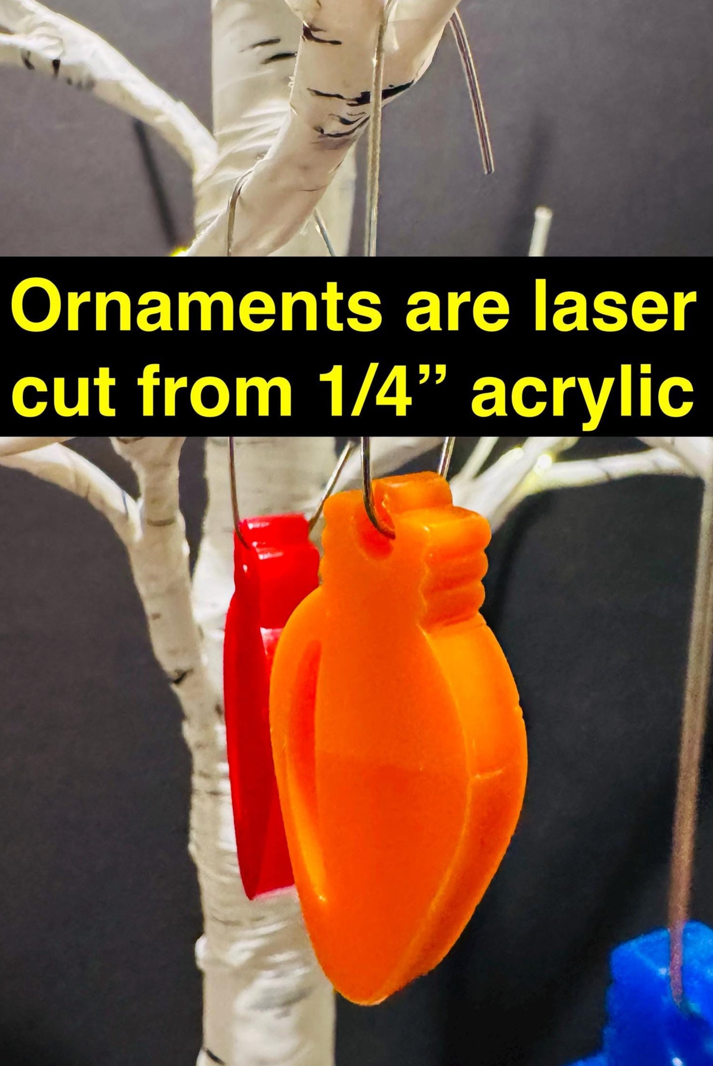 Orange and red acrylic ornaments on a white tree branch with text about material quality.